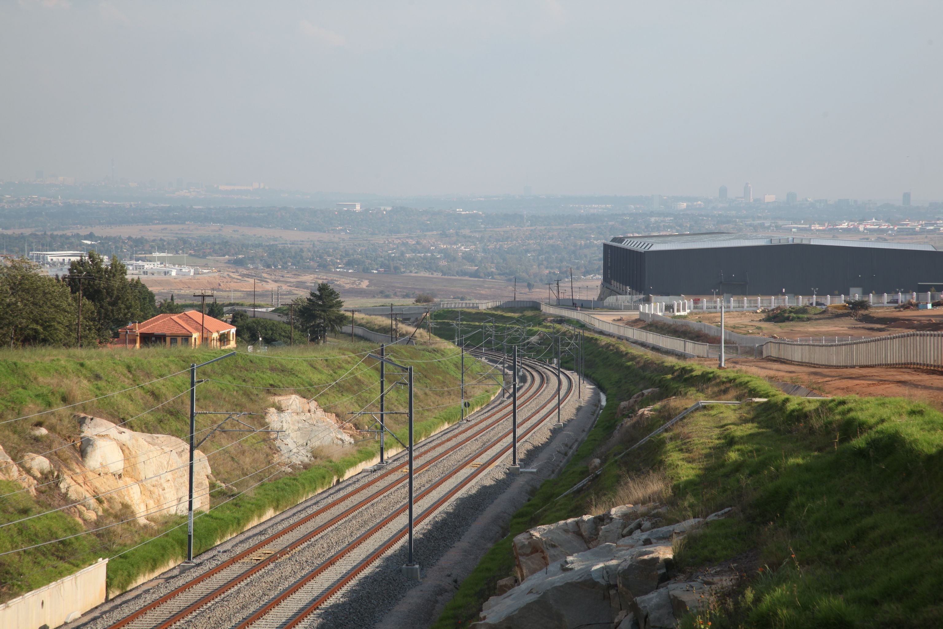 Gautrain railway tracks curving through a cutting in Midrand, with the Gauteng landscape and distant skyline beyond