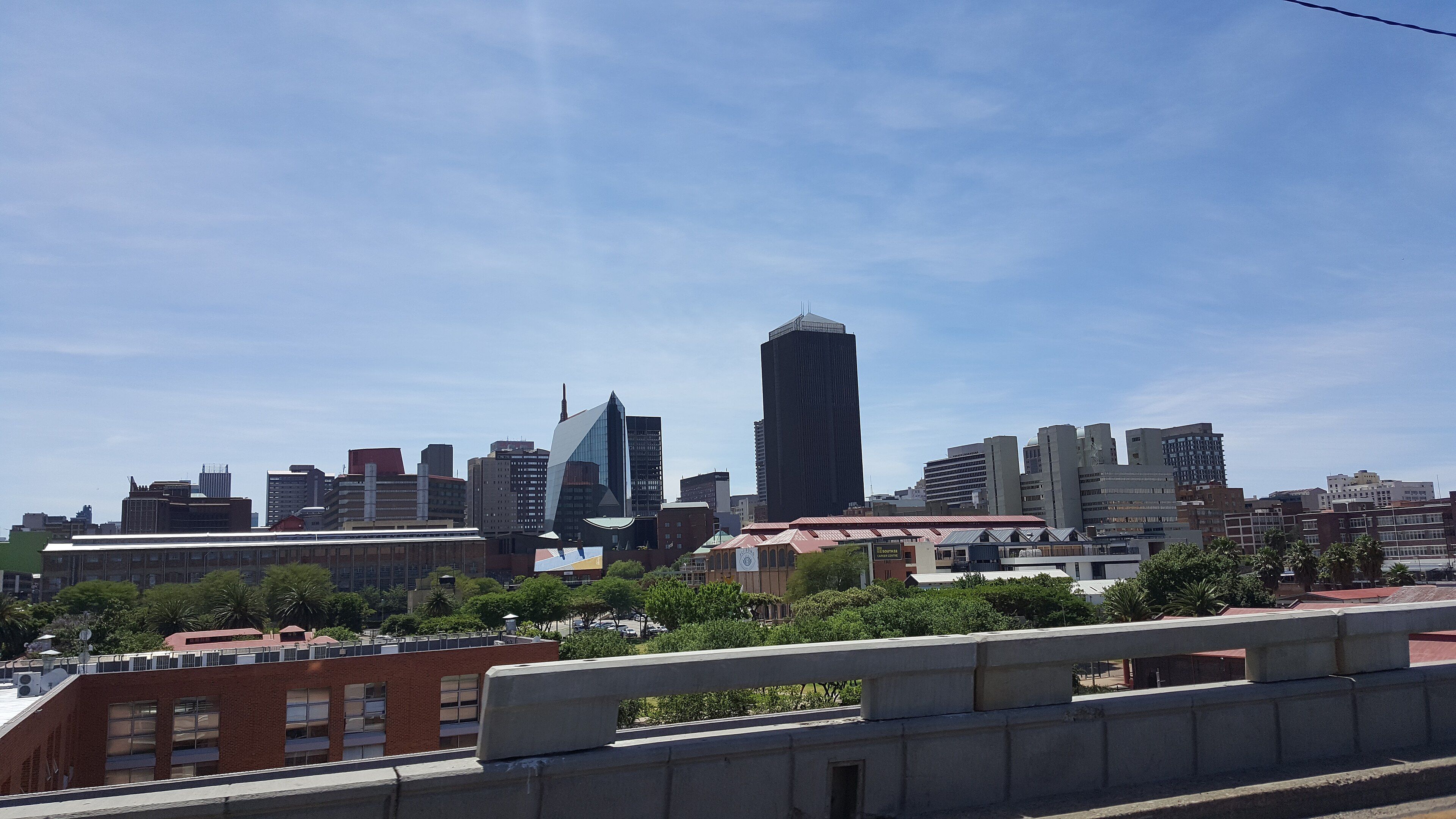 Johannesburg city centre skyline seen from Newtown, with low brick buildings and trees in the foreground